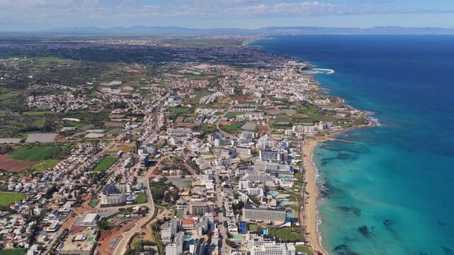 Aerial drone view of Protaras and Paralimni coastline, Cyprus, showing long sandy beaches, turquoise sea, and dense urban development stretching along the Mediterranean shore