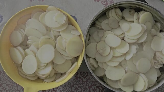 Freshly sliced potatoes are being boiled in hot water, releasing visible steam that rises gently into the air. 