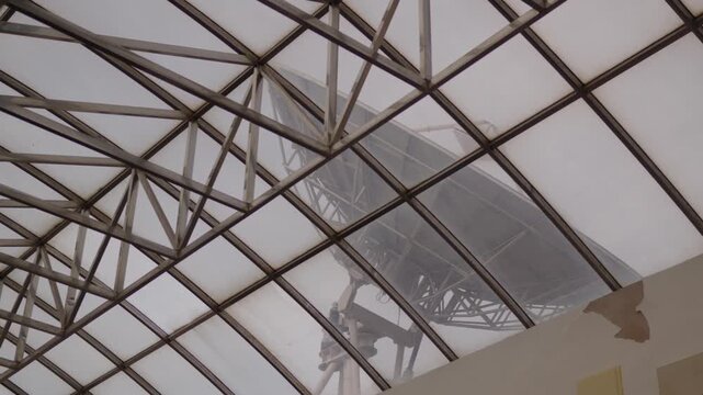 Television broadcast tower with antenna arrays visible behind glass atrium structure, emphasizing signal transmission systems, media infrastructure integrated into modern urban communication networks
