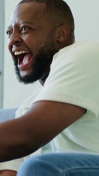Vertical video: Reacting to game, boy holding white controller, dad cheering on couch, copy space