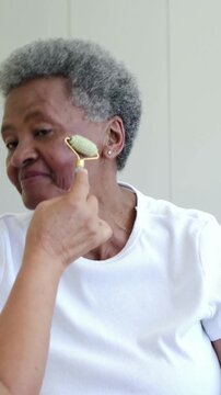 Vertical video: Sitting woman in white tee at home receiving green roller as helper rolling jaw