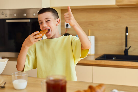 Happy boy eating croissant giving thumbs up