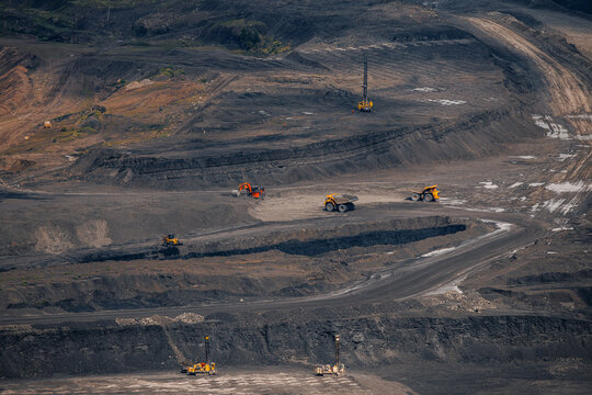 Expansive open pit mine with heavy machinery extracting resources, excavator loading coal, drilling rig working with detonator
