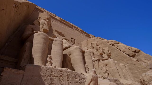 Close-up of giant Ramesses II colossi carved into rock facade at Abu Simbel temple, Egypt. Dramatic upward view of ancient sandstone pharaoh statues. Travel and history.