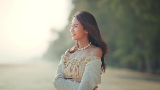 A beautiful young Asian woman smiling happy on a tropical beach during sunset, wearing a stylish off-shoulder, embodying summer vacation vibes, freedom, and wellness for travel and lifestyle concepts.