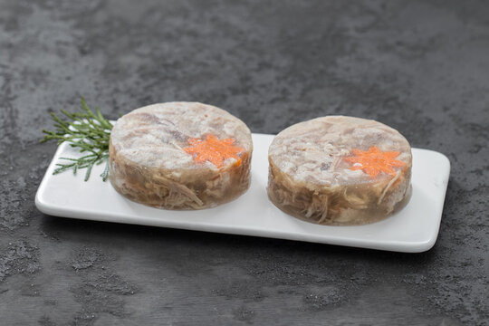 Russian cold appetizer. Pork Aspic. Decorated with carrot flower. On a plate. Dark gray background	
