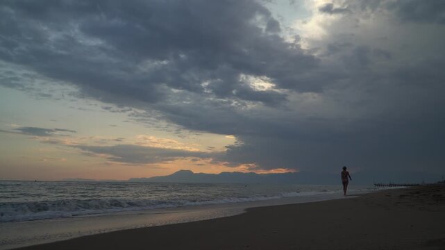 Tourist woman walking on Antalya beach at sunset, Mediterranean coast Turkey.