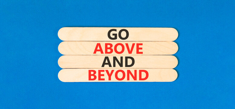 Go above and beyond words symbol. Concept words Go above and beyond on beautiful wooden sticks. Beautiful blue background. Business motivational Go above and beyond concept. Copy space.