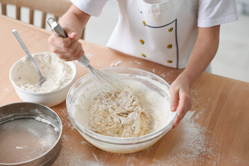 Fototapeta premium Child mixing dough in bowl at wooden table indoors, closeup