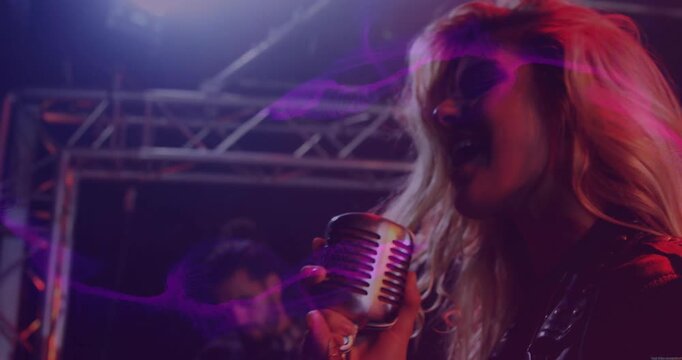 Lead singer starting song on music stage, leaning into mic while purple streaks revealing guitarist