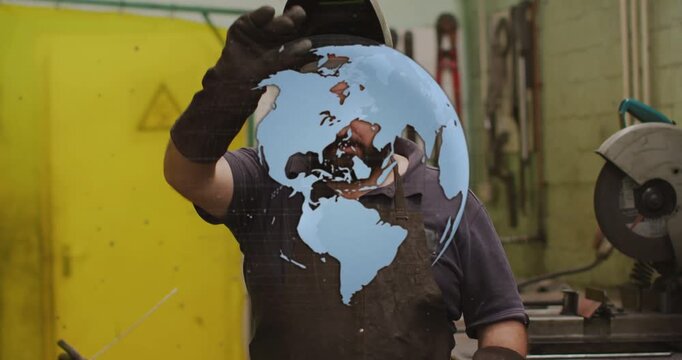 Welder lifting helmet in metal shop as blue globe shifting revealing face, gloves crossing chest