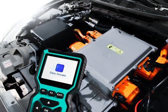 Electric Car Diagnostic Scanner, A teal diagnostic scanner shows Data Stream while held over a modern electric car engine with orange high-voltage cables in a workshop.