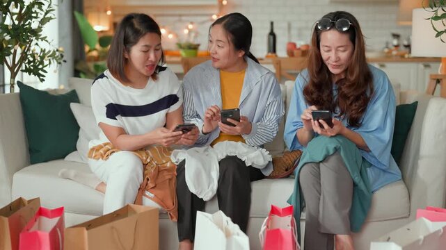 Three Asian women friends relaxing after shopping, sitting on sofa with bags, chatting and sharing life stories, happy summer sale lifestyle, casual leisure, bonding, joy and modern home living room m