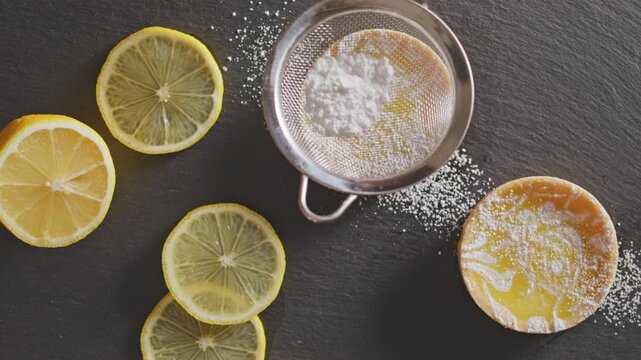Lemon tarts dusted with powdered sugar, garnished with citrus slices on a dark backdrop.