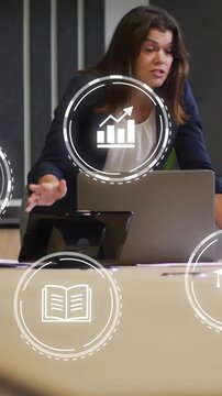 Mid-adult woman blazer leading meeting table after peer cue, pointing at laptop, phone, chart icons