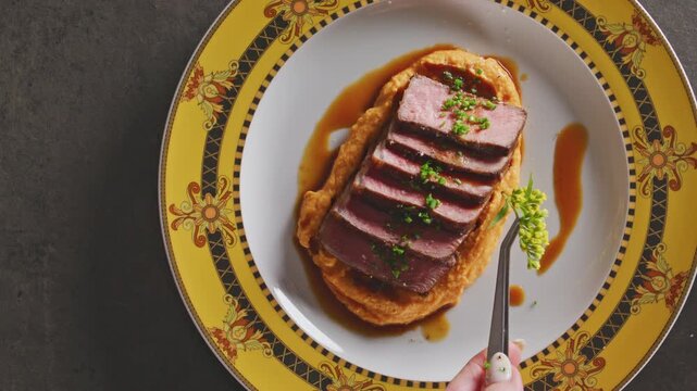 Chef garnishes a plated NY strip steak with fresh herbs and chives using tweezers.