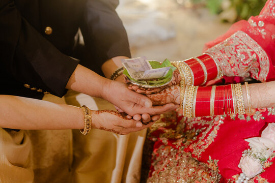 Close-up of traditional Indian wedding ritual with couple's hands, currency, and auspicious elements symbolizing blessings and prosperity