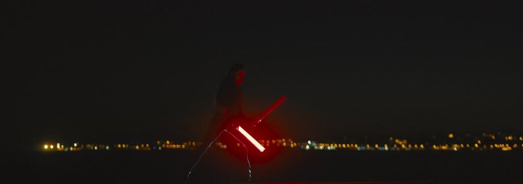 Woman performing a light show with red batons at night