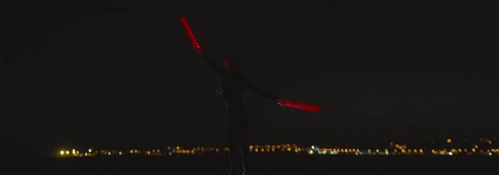 Silhouette of a woman juggling with glowing red lights at night