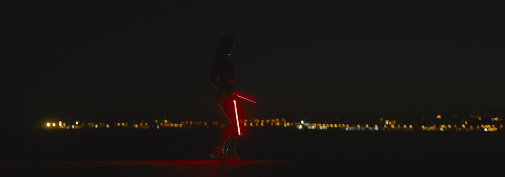 Woman performing a dance routine with red glowing led batons at night