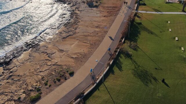 Aerial drone view of cyclists riding along coastal path in Ayia Napa, Cyprus at sunset