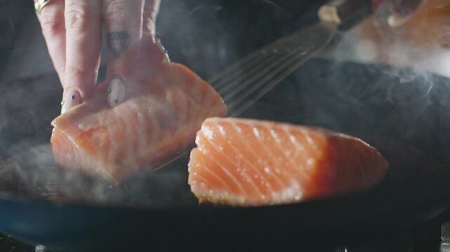 Salmon fillets flipped in a frying pan with a spatula.