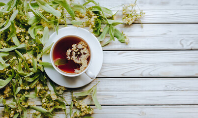 White cup of linden tea on linden blossom background. Herbal medicine. Top view. Treatment of cold and flu.