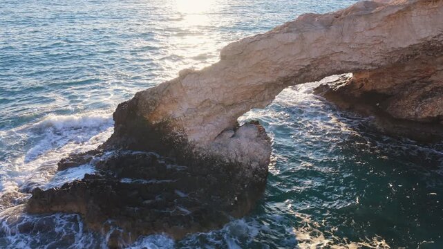 Aerial drone view of the Bridge of Love, a natural rock arch formation in Ayia Napa, Cyprus. Turquoise waves flow beneath the limestone arch