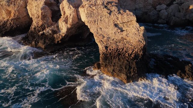 Aerial drone view of the Bridge of Love, a natural rock arch formation in Ayia Napa, Cyprus. Turquoise waves flow beneath the limestone arch