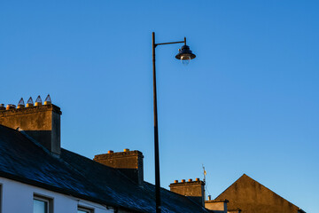 Obraz premium Street Lamp Above Rooftops in Ireland Against Clear Blue Sky at Sunset