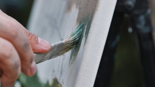 Artist painting en plein air, applying green paint to canvas outdoors in Moscow
