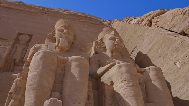 Close-up of giant Ramesses II colossi carved into rock facade at Abu Simbel temple, Egypt. Dramatic upward view of ancient sandstone pharaoh statues. Travel and history.