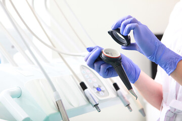 Fototapeta premium Sandblasting teeth cleaning. Female dentist's hand in blue gloves holding sandblasting tool. Сoncept of dentistry and dental care. Oral hygiene. Prevention of dental diseases.
