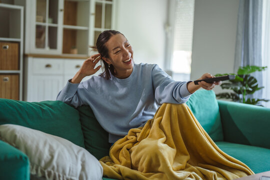 Asian woman laughing watching television using remote control
