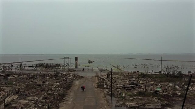 Aerial perspective flying over the Villa Epecuen resort ruins towards the water. Threatening atmosphere of storm and total destruction.