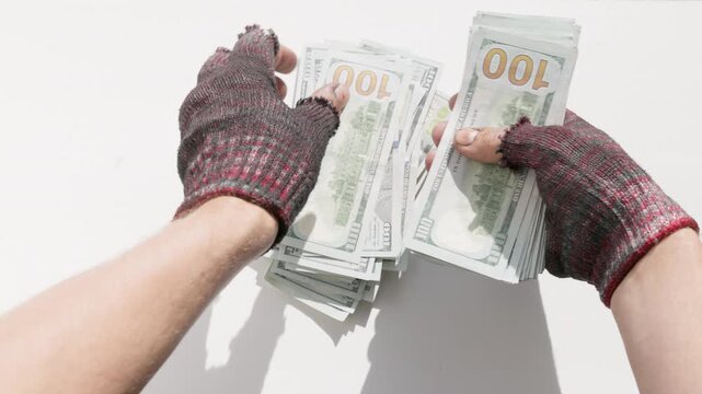 Homeless person's hands wearing fingerless gloves count a large stack of 100-dollar banknotes. High angle first person view,