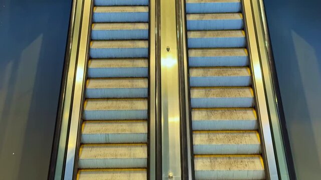 Two escalators are shown in a public area, one escalator is moving while the other is not. People may be nearby but are not visible in this view.