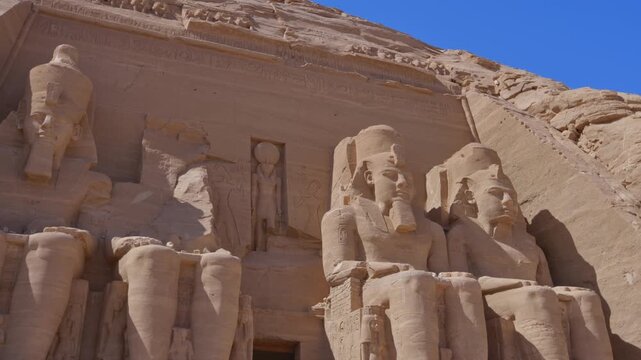 Close-up of giant Ramesses II colossi carved into rock facade at Abu Simbel temple, Egypt. Dramatic upward view of ancient sandstone pharaoh statues. Travel and history.
