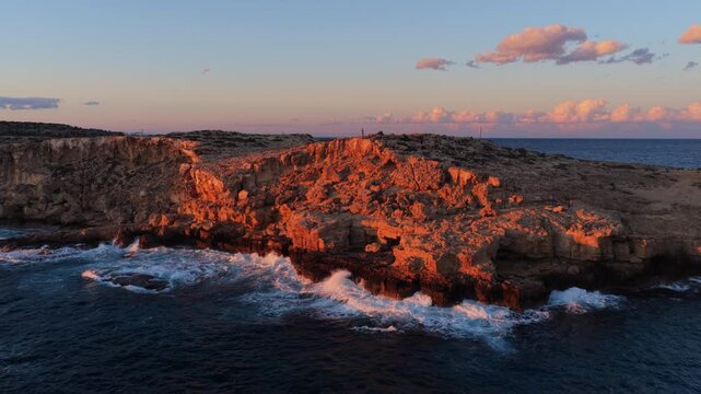 Aerial drone view of rugged coastal cliffs in Cape Greco, Cyprus, illuminated by warm sunset light