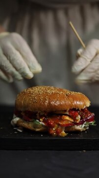 A woman prepares homemade burgers in a kitchen, cooking and assembling fresh ingredients in a process that reflects both home kitchen and professional restaurant-style cooking.