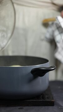 A female cook opens a pot to check boiling pasta, capturing an authentic cooking process suitable for both home kitchens and professional restaurant environments.