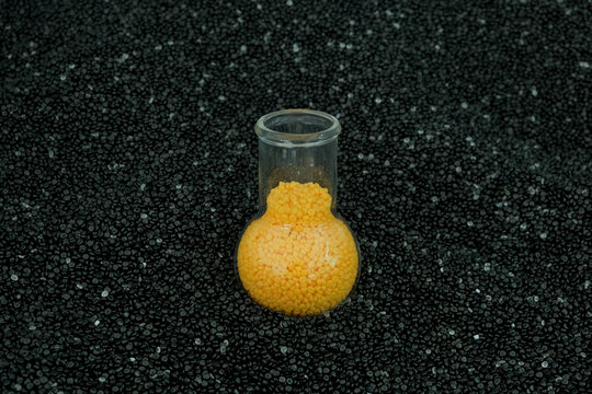 Yellow coloured polyethylene granules in glass flask on black and white PE pellets backgground. Granulated plastic polymer, masterbatch. Experiments with color
