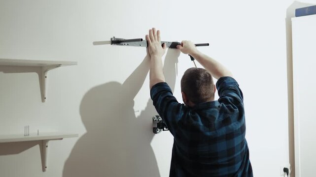 Close up of man installing wooden wall shelf with electric drill, DIY home improvement project, 4K footage.