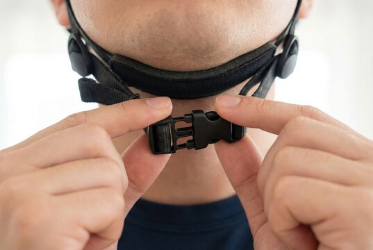 Hands snapping the black plastic buckle of a safety helmet strap under the chin