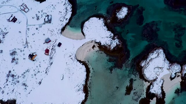 Top-Down Drohnenflug &uuml;ber schneebedeckte Inseln mit Holzh&auml;usern und t&uuml;rkisfarbenem Meer in Sommar&oslash;y, Nordnorwegen, 4K