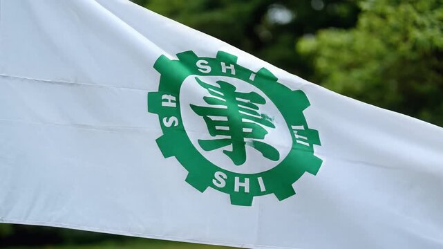 White flag with green gear logo and Japanese characters waving in the wind.