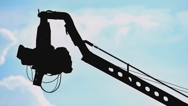 Professional cinema camera on a crane arm, silhouetted against a pale blue sky