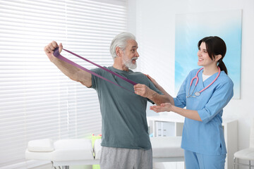 Fototapeta premium Senior man training with resistance band under physiotherapist supervision indoors