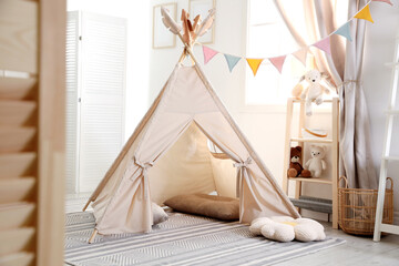 Stylish toy wigwam, furniture, pillows and decor in light playroom. Interior design © New Africa