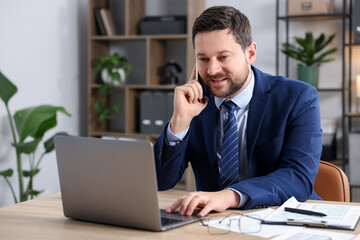 Obraz premium Man talking on smartphone at wooden desk indoors
